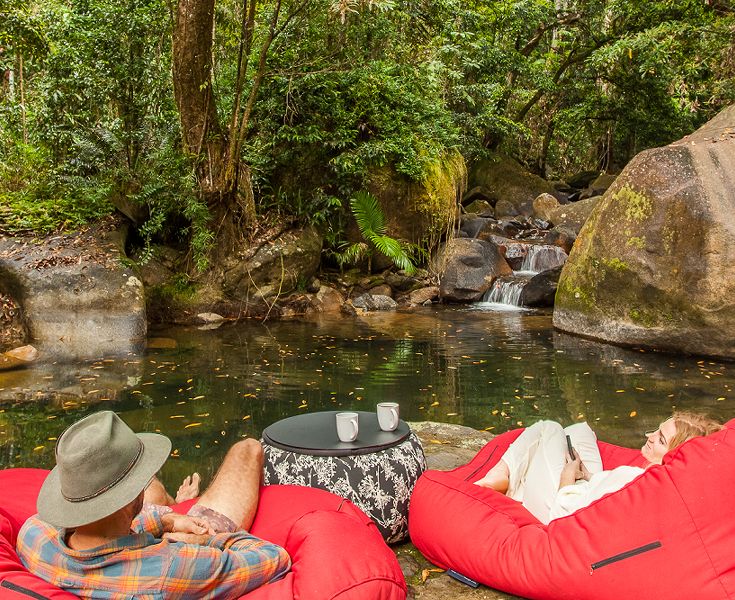 A traveling couple relaxing by the edge of the private freshwater swimming hole steps from the residential veranda