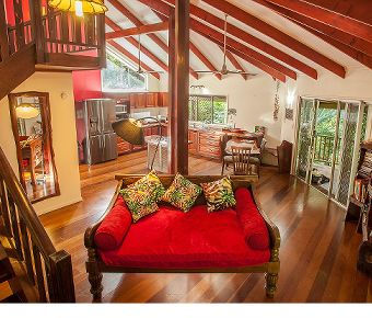 Open plan living room with high ceilings, fully equipped kitchen, dining area, and sliding doors to the veranda deck.