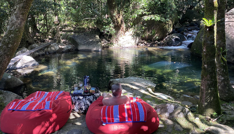 Guest lounging by the crystalline private swimming hole in a large outdoor bean bag chair