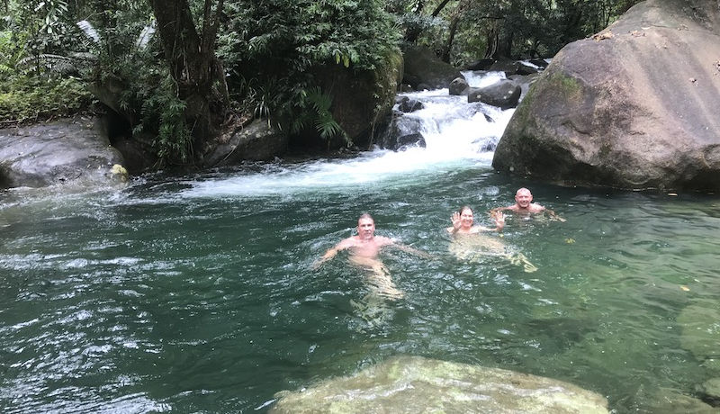 Swimmers enjoying clear mountain waters directly beneath the private waterfall cascades